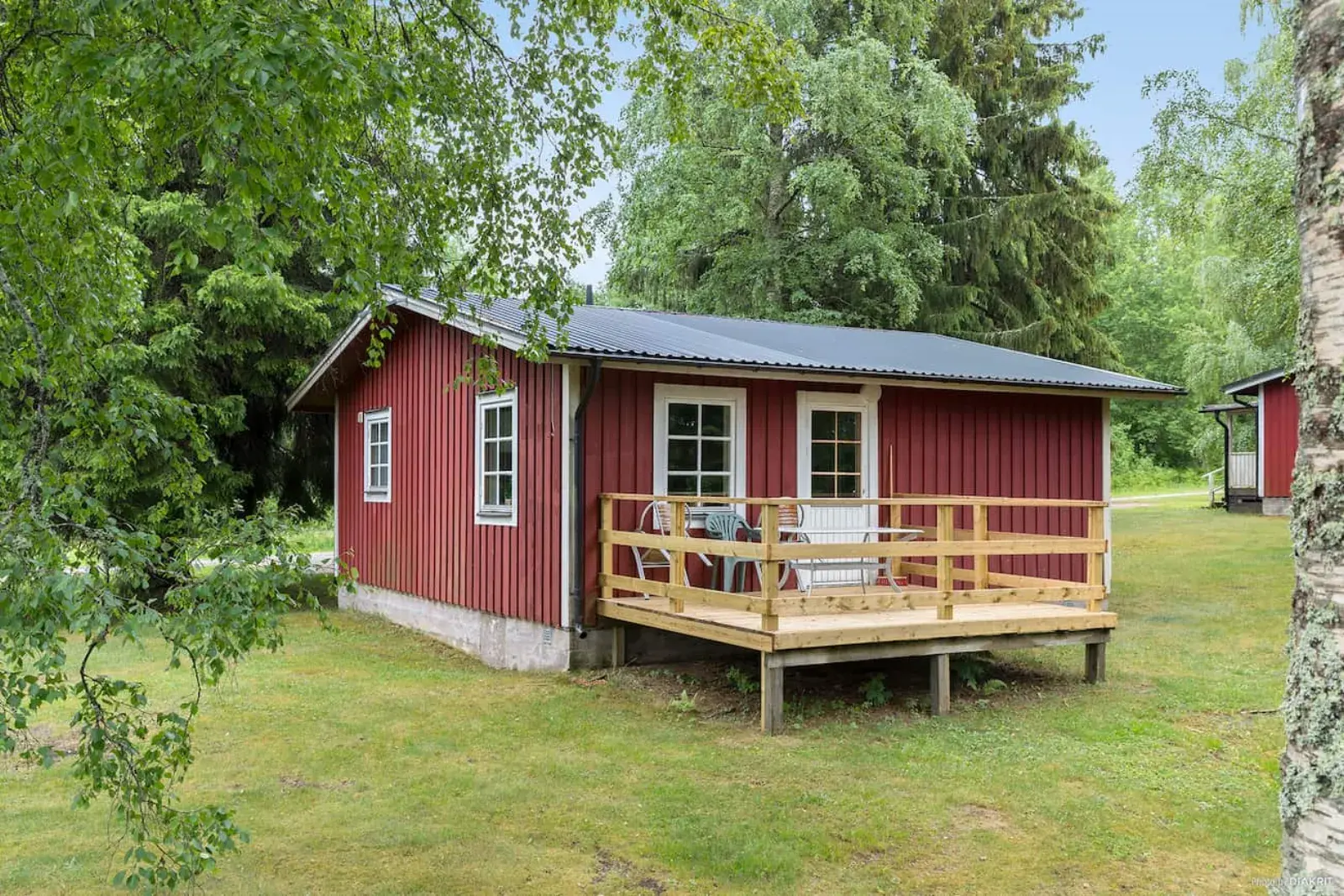 Red cabin with a deck on the lawn among the trees