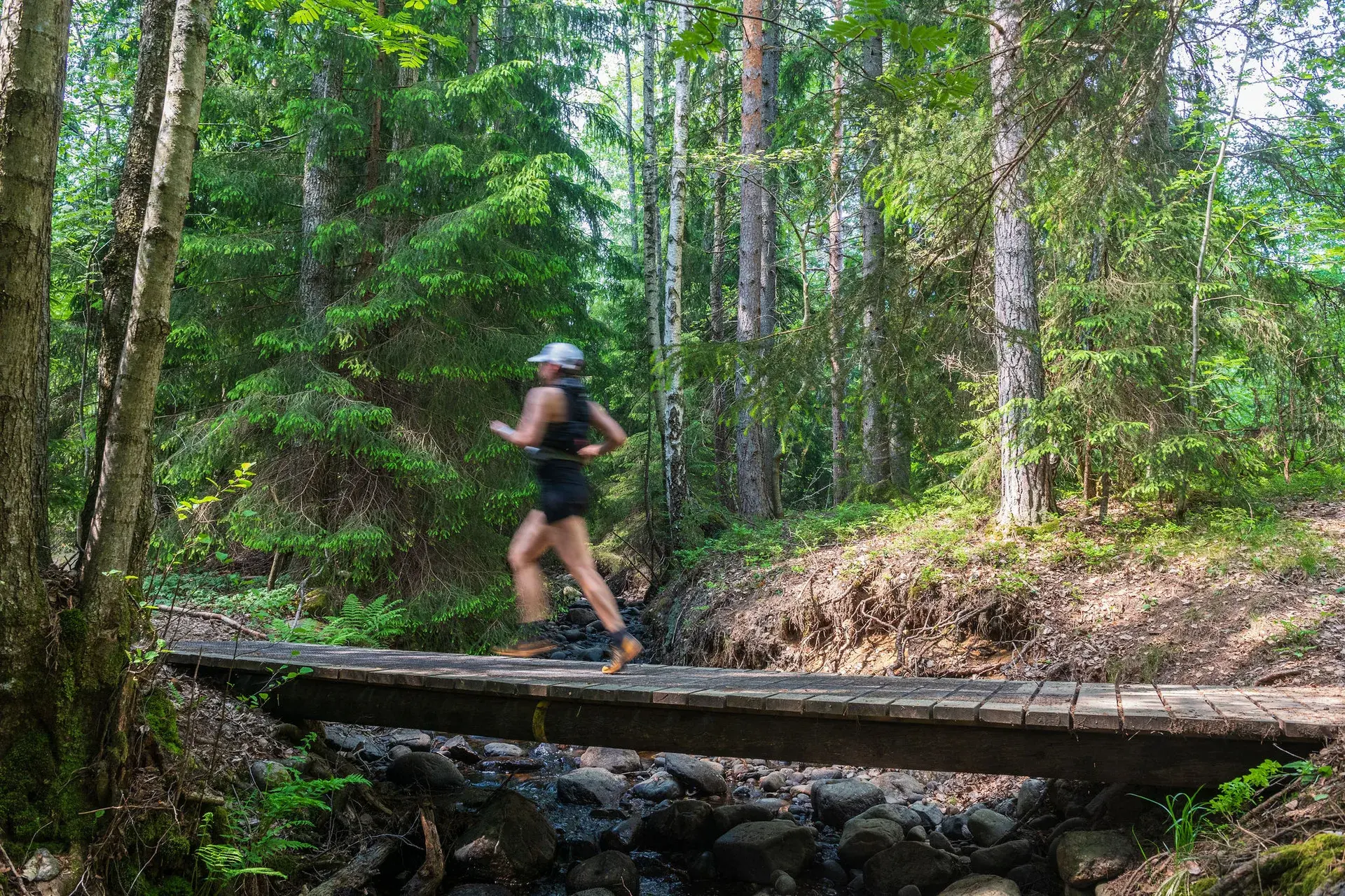 Löpare i rörelse över spången, med bäcken och stenarna under, 2024