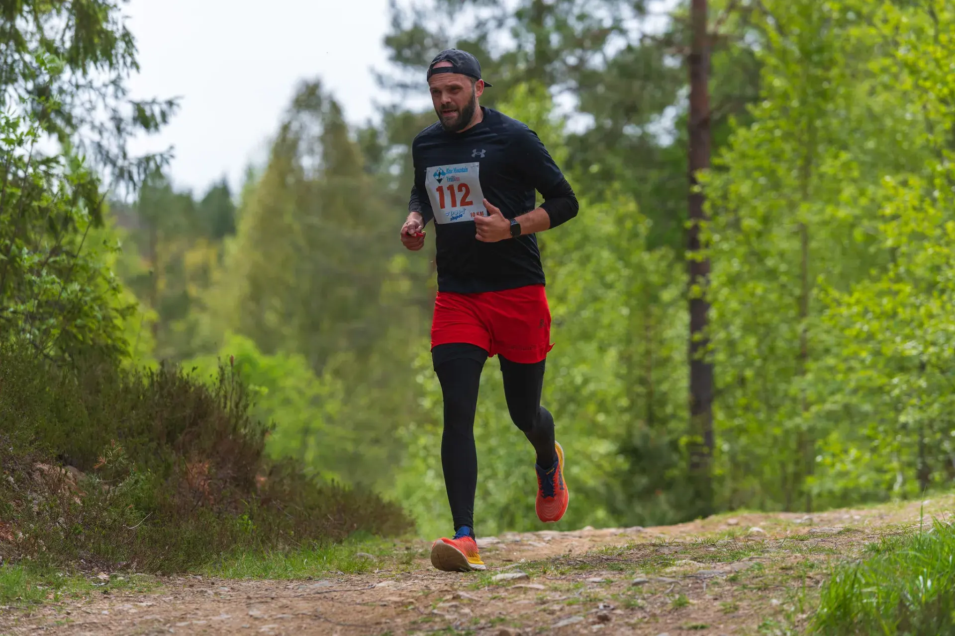 Löpare i röda shorts kommer över krönet på en grusig stig, 2025