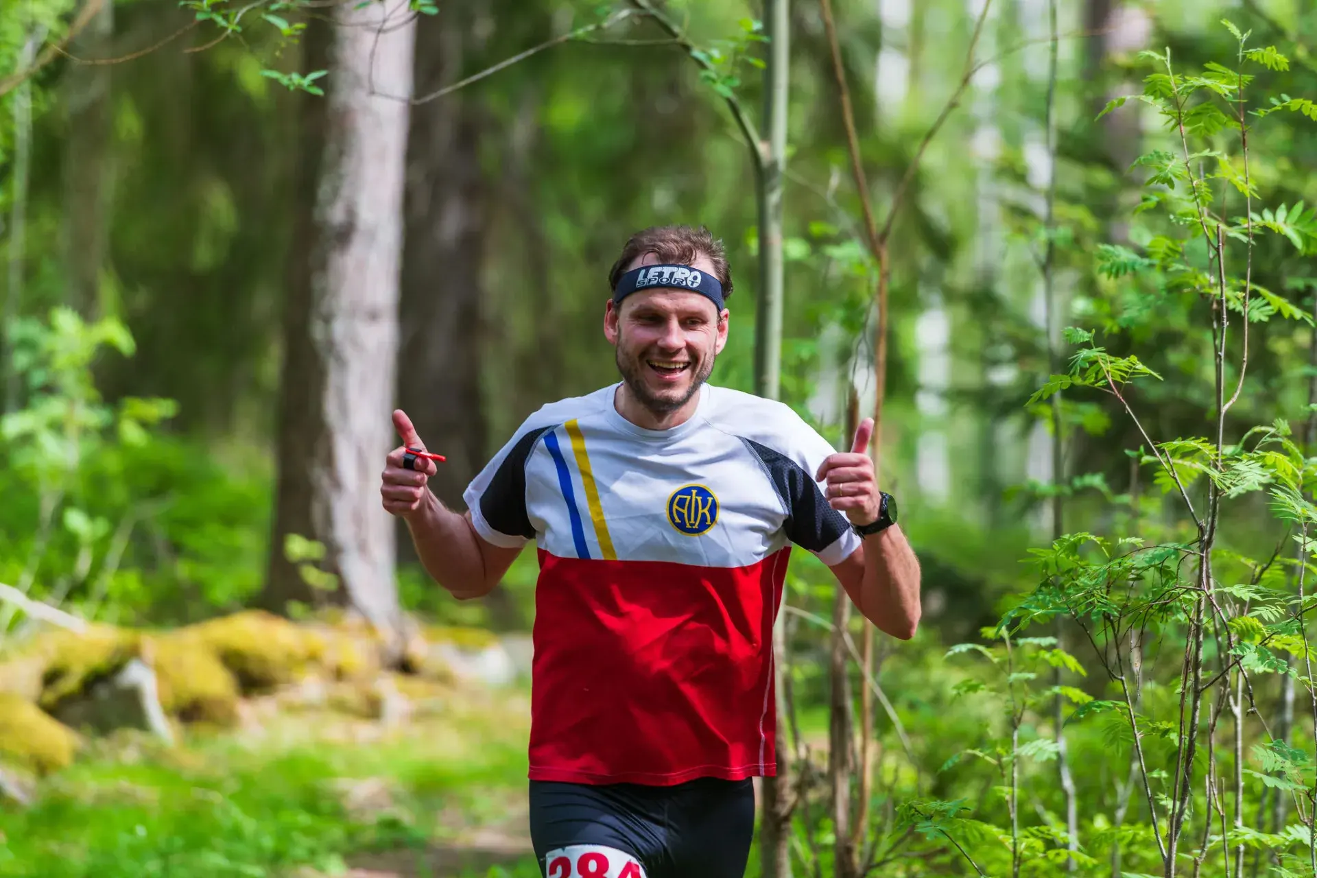 Glad löpare gör tummarna upp i lövskogen, 2025